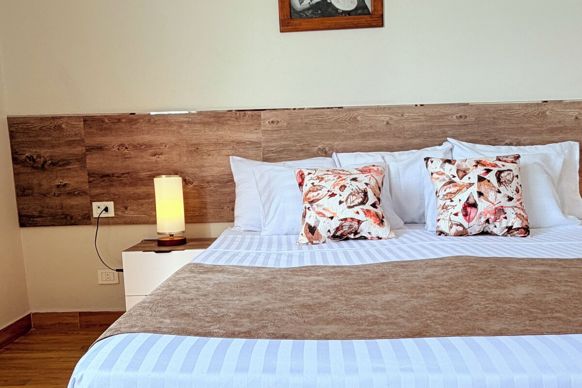Een netjes opgemaakt bed met een houten hoofdeinde, witte kussens en een plaid met bloemenprint.