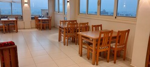 A dining area with wooden tables and chairs, large windows with city views, and a tiled floor. - Eco Green Hotel (Giza)