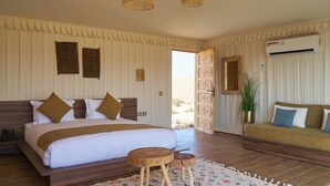 A bedroom with a large bed, a wooden bench, a patterned rug, and a view of the desert through an open door. - Stellar Desert Camp (Marrakech)