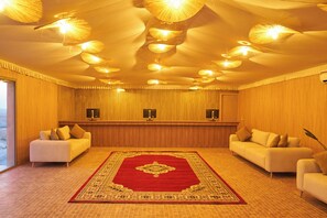A hotel room with a large red carpet, two sofas, a wooden reception desk, and ceiling lights. - Stellar Desert Camp (Marrakech)