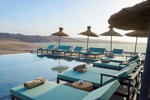 An infinity pool with lounge chairs and thatched umbrellas, overlooking a desert landscape. - Stellar Desert Camp (Marrakech)