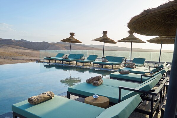 An infinity pool with lounge chairs and thatched umbrellas, overlooking a desert landscape. - Stellar Desert Camp (Marrakech)