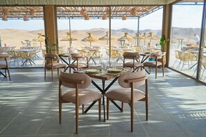 An outdoor dining area with tables and chairs, a view of the desert landscape, and a pergola with hanging lights. - Stellar Desert Camp (Marrakech)