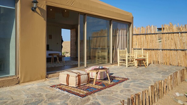 A desert tent with a stone patio, a wooden fence, and a view of the desert. - Stellar Desert Camp (Marrakech)