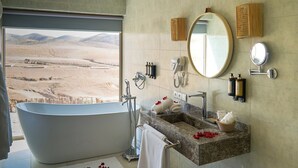 A bathroom with a large bathtub, a sink, and a mirror. There are towels and toiletries on the counter. - Stellar Desert Camp (Marrakech)