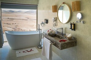 Un baño con una bañera grande, un lavabo y un espejo. Hay toallas y artículos de aseo en la encimera.
