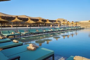 A poolside area with lounge chairs and thatched umbrellas, a clear sky, and a desert landscape in the background. - Stellar Desert Camp (Marrakech)