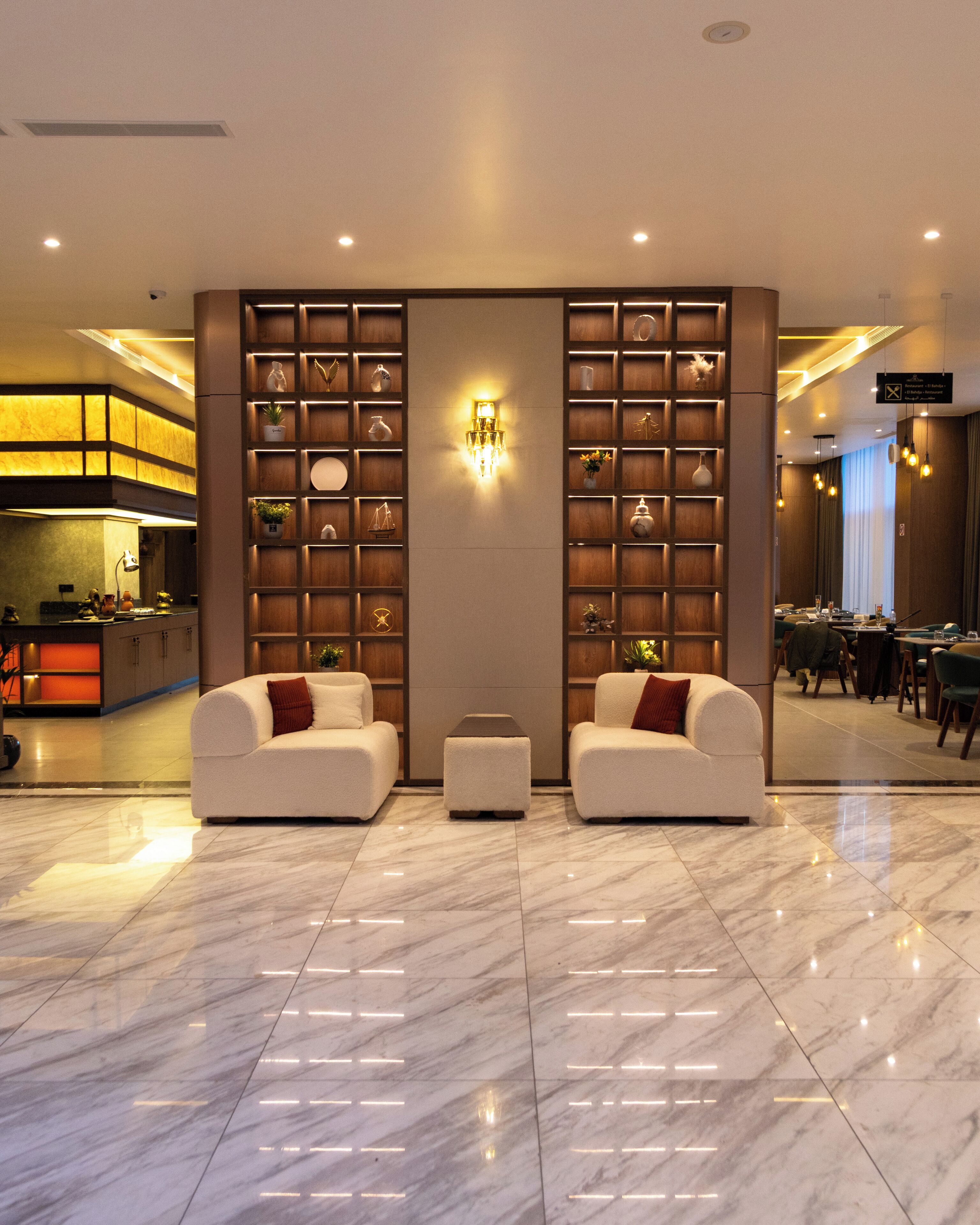 A modern lobby with two white sofas, a central light fixture, and a marble floor.