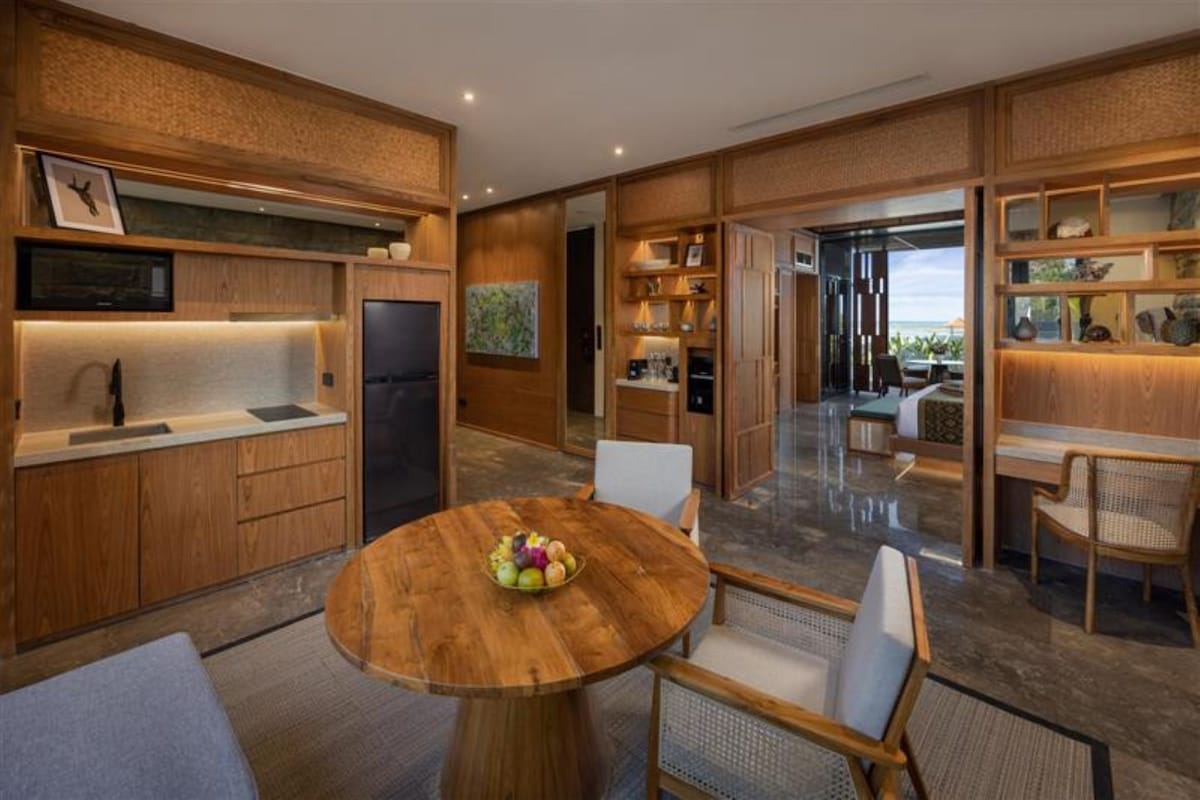 Une cuisine moderne avec des meubles en bois, une table ronde en bois ornée de fruits et une vue sur l’extérieur.