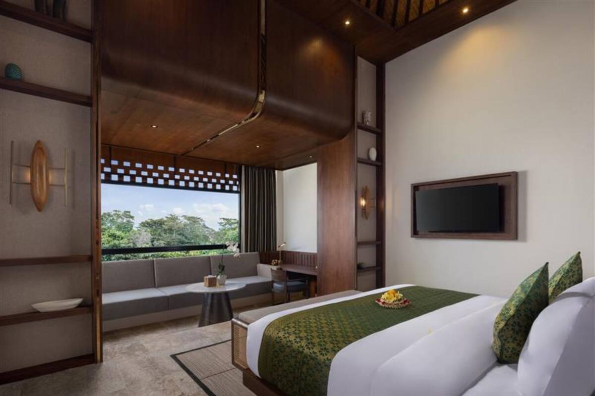 Une chambre d’hôtel moderne dotée d’un grand lit, d’un coin salon, d’une télévision et offrant une vue sur la verdure environnante.