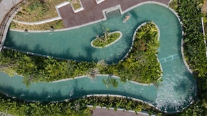 Vue aérienne d’un espace piscine aménagé, avec des allées sinueuses et une végétation luxuriante tout autour.
