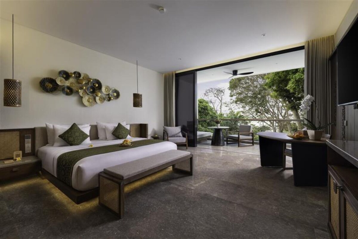 Een moderne hotelkamer met een groot bed, een zithoek en een balkon met uitzicht op bomen.