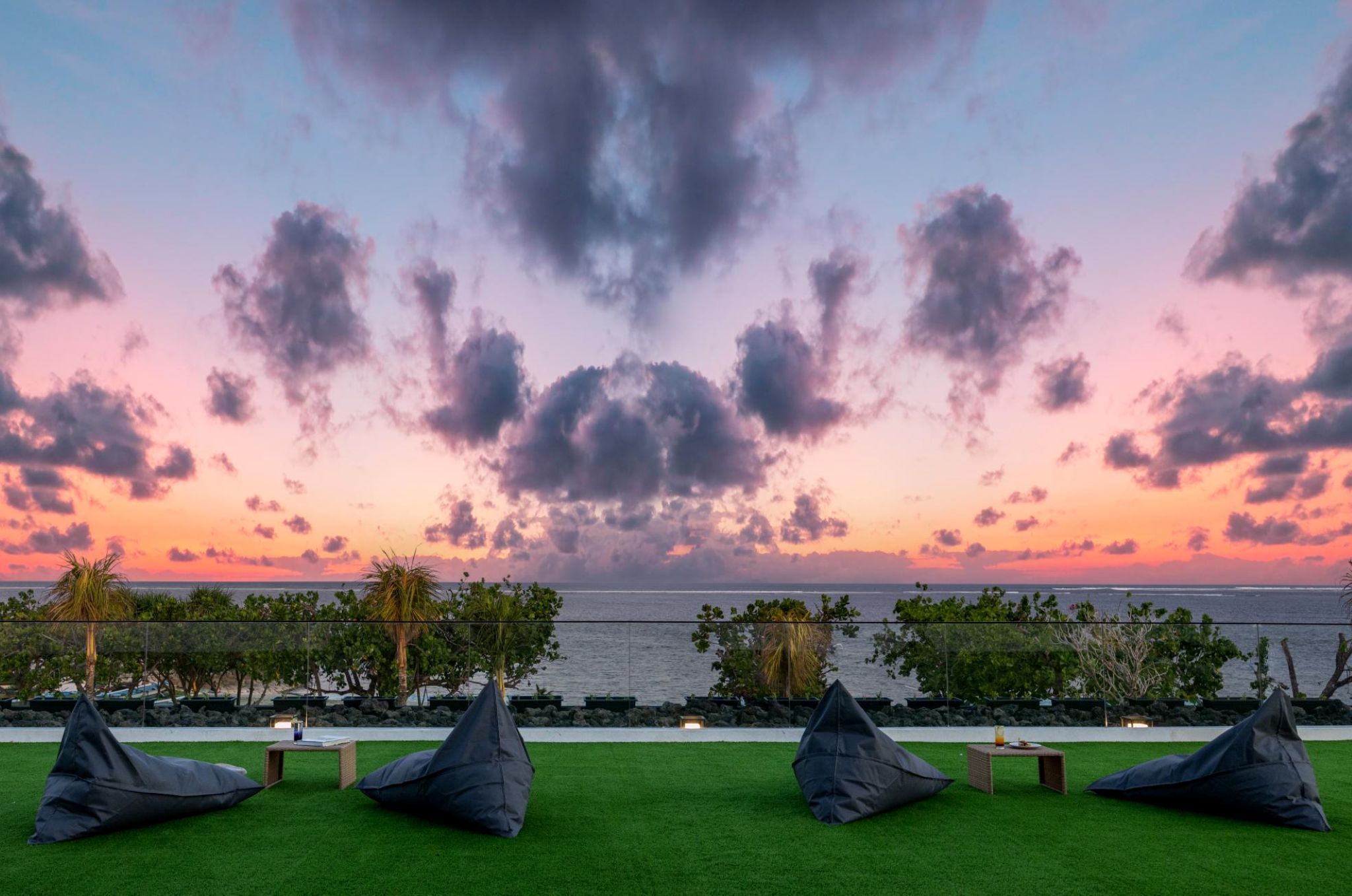 A sunset view with beach chairs and tables on a grassy area.