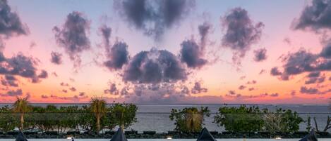 A sunset view with beach chairs and tables on a grassy area.