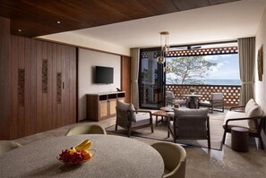 Een moderne hotelkamer met een groot raam met uitzicht op de zee, een eetgedeelte met een ronde tafel en een zithoek met stoelen en een bank.
