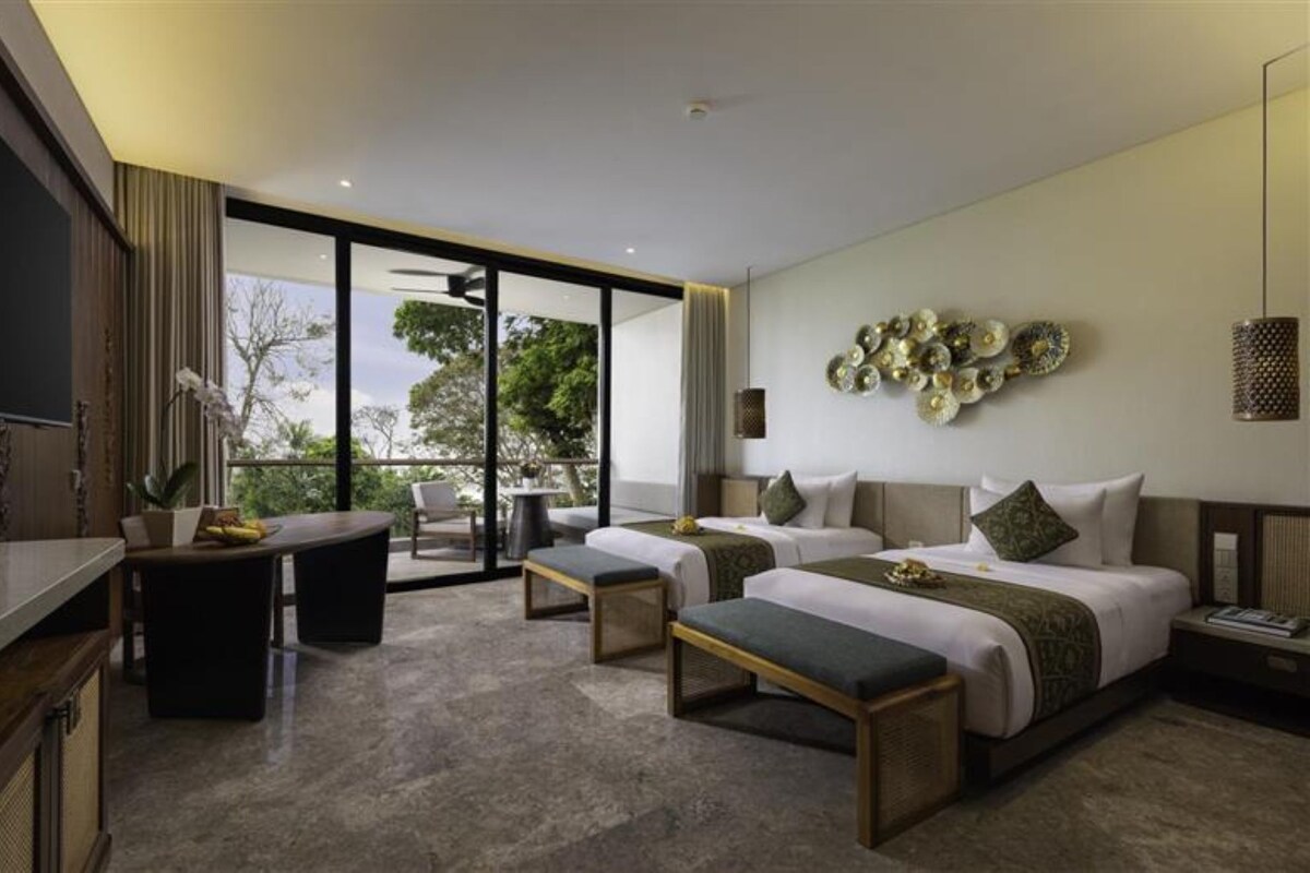 Een moderne hotelkamer met een groot bed, twee nachtkastjes, een bureau en een balkon met uitzicht op bomen.