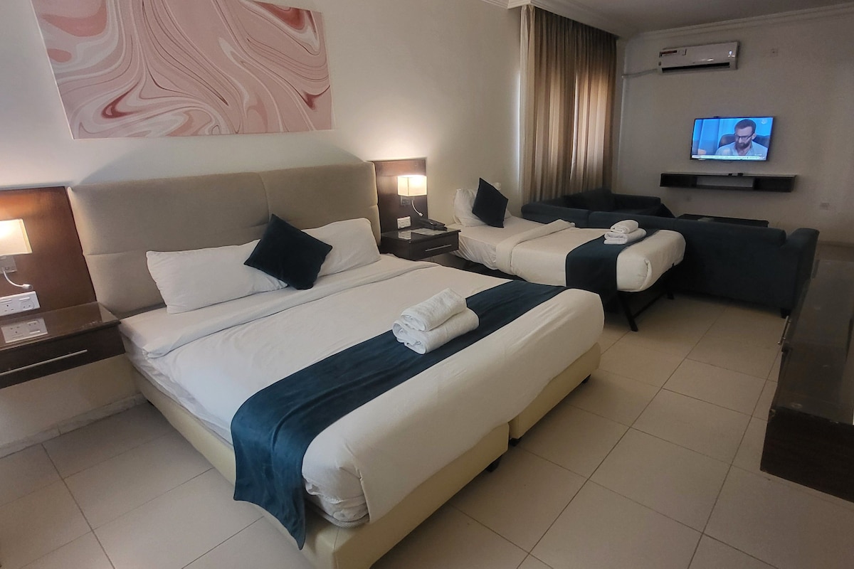 Habitación de hotel con dos camas, un sofá, un televisor y una cafetera.