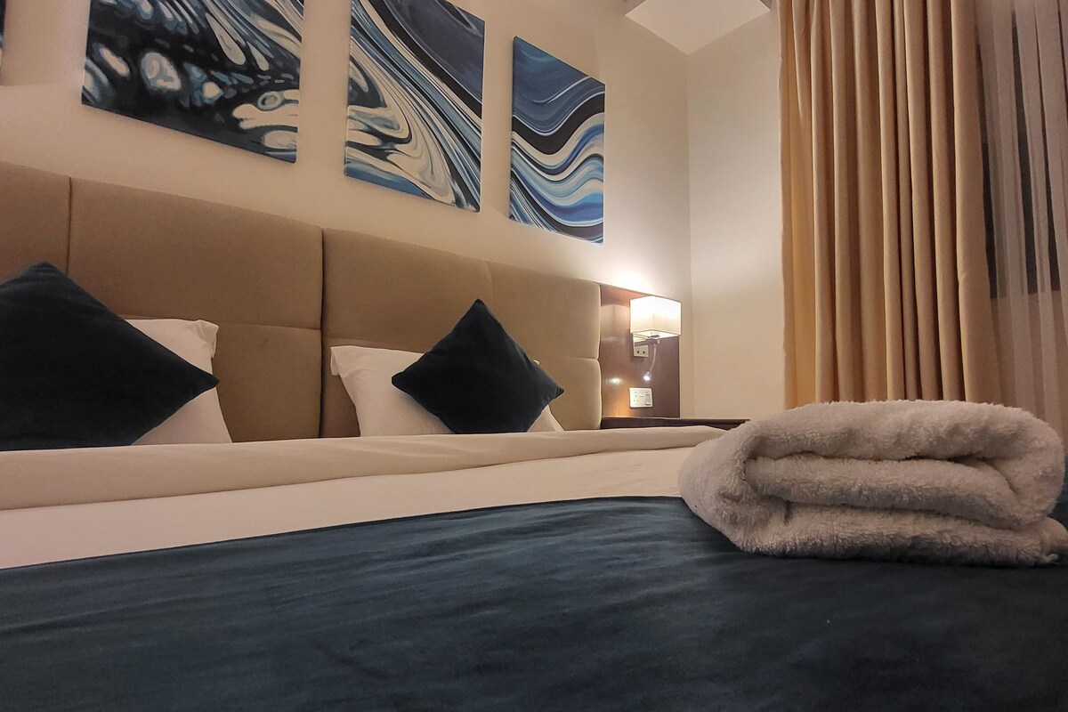 Habitación de hotel con cama, cabecera y tres cuadros abstractos en la pared.