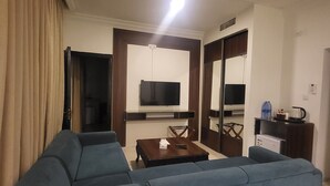 A living room with a sofa, a coffee table, a TV mounted on the wall, and a door leading to another room. - Jordan View Hotel (Amman)