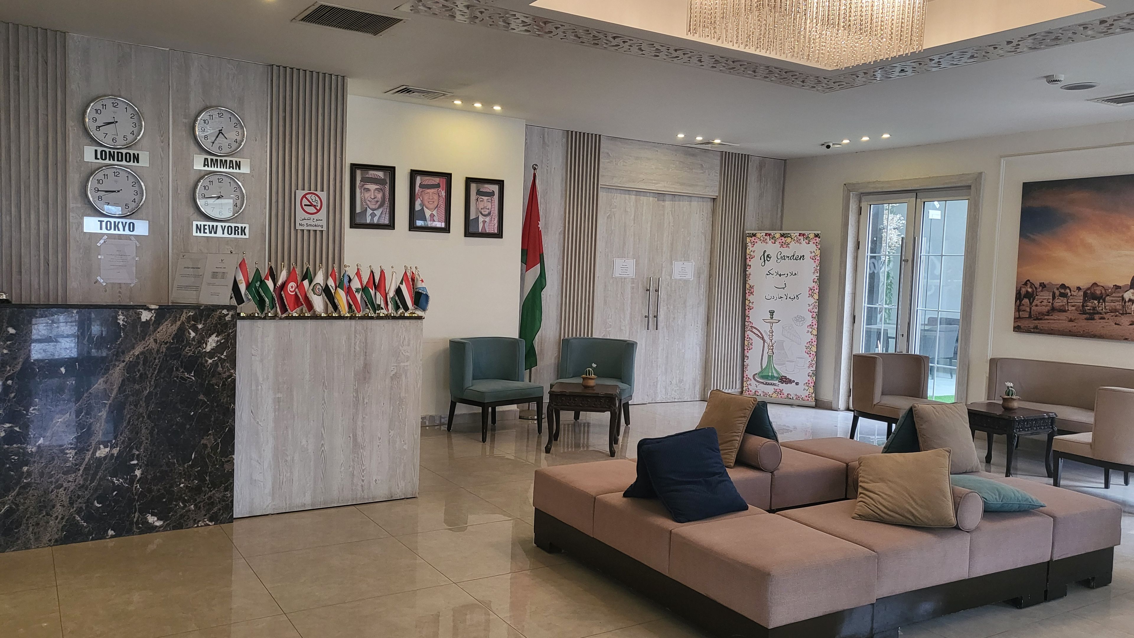 Un vestíbulo con un mostrador de recepción que exhibe banderas internacionales, relojes mostrando diferentes husos horarios y un cuadro grande de un paisaje desértico.