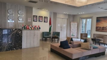 Un vestíbulo con un mostrador de recepción que exhibe banderas internacionales, relojes mostrando diferentes husos horarios y un cuadro grande de un paisaje desértico.