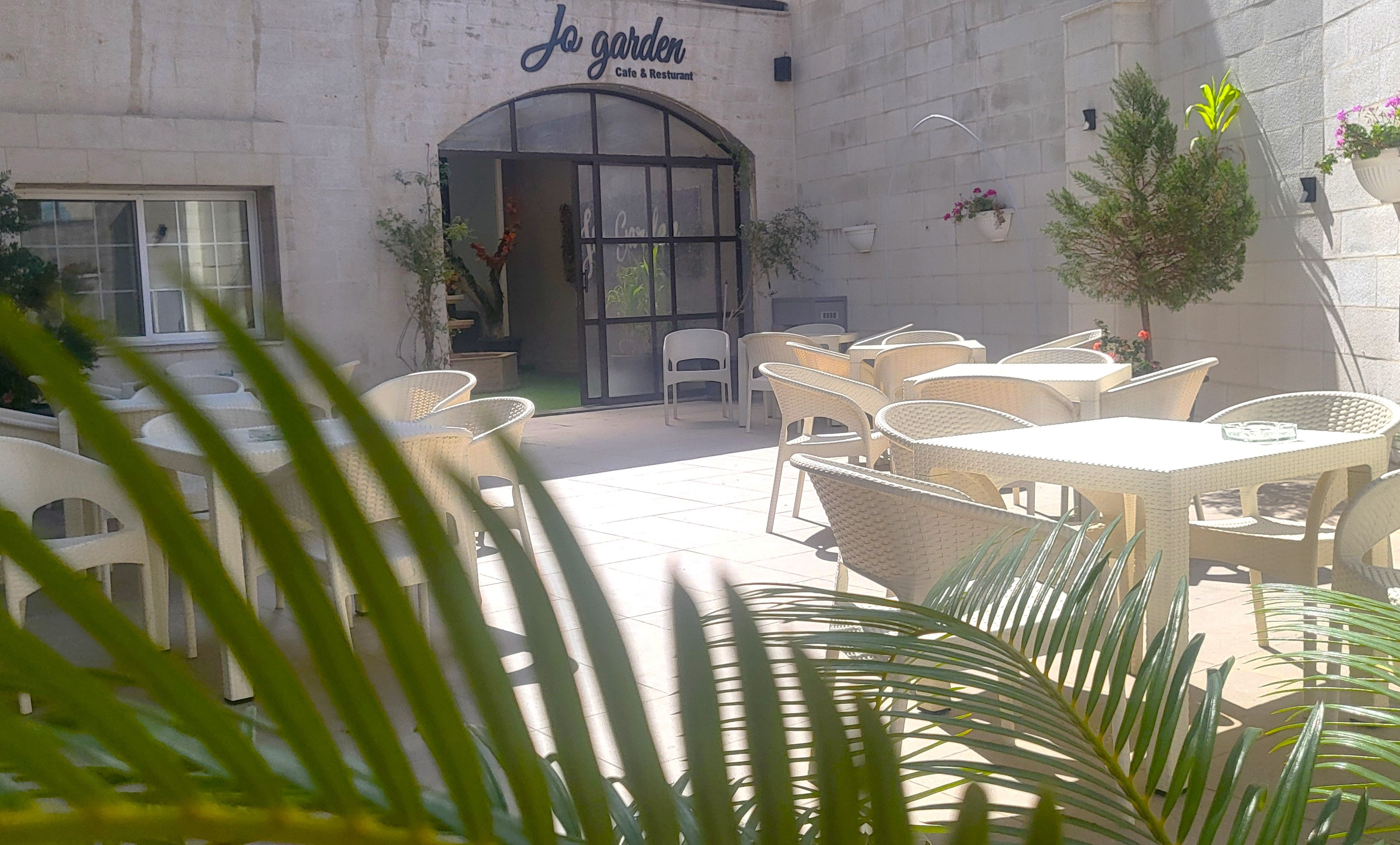 An outdoor seating area with wicker tables and chairs, a cafe entrance, and potted plants.