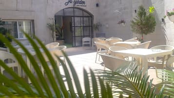 An outdoor seating area with wicker tables and chairs, a cafe entrance, and potted plants.