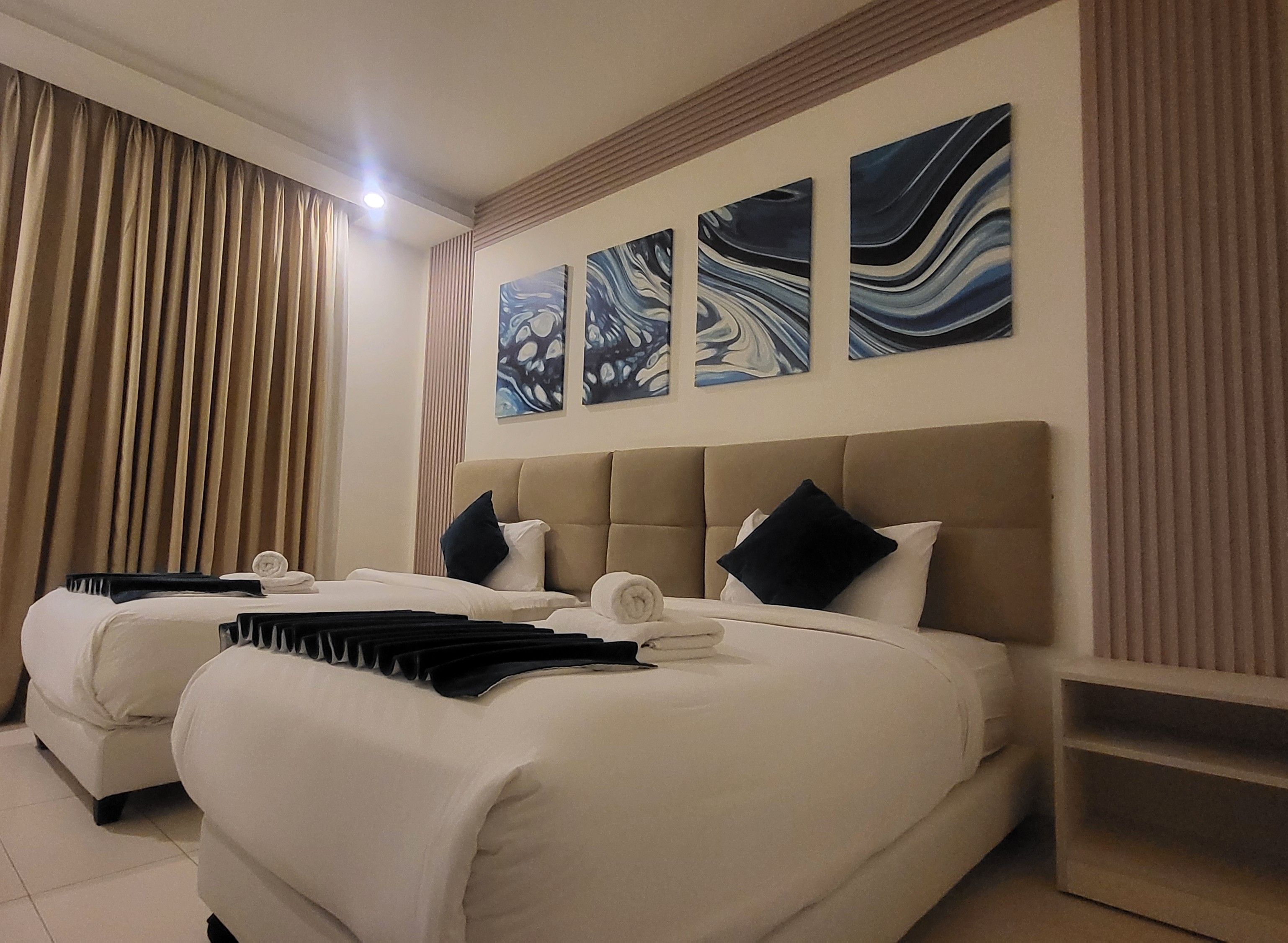 Habitación de hotel con dos camas, cabeceros color beige y tres pinturas abstractas en la pared.