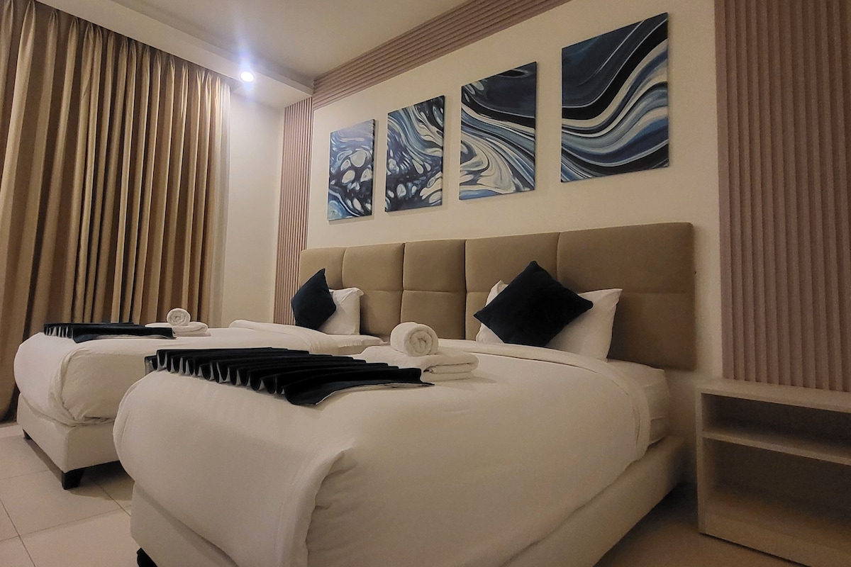 Habitación de hotel con dos camas, cabeceros color beige y tres pinturas abstractas en la pared.