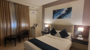 Una habitación de hotel con cama, escritorio, silla y un cuadro en la pared.
