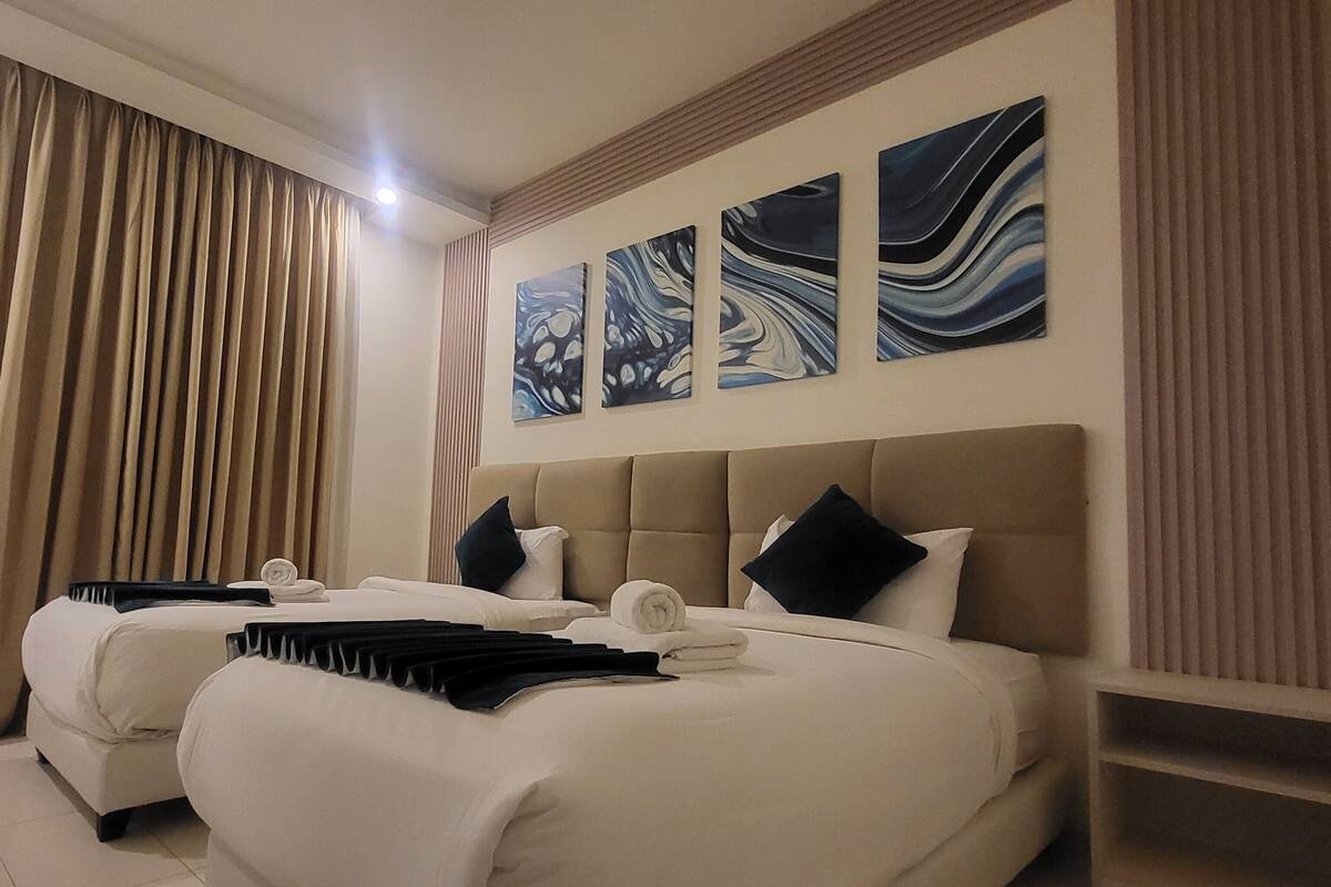 Habitación de hotel con dos camas, cabeceros color beige y tres pinturas abstractas en la pared.