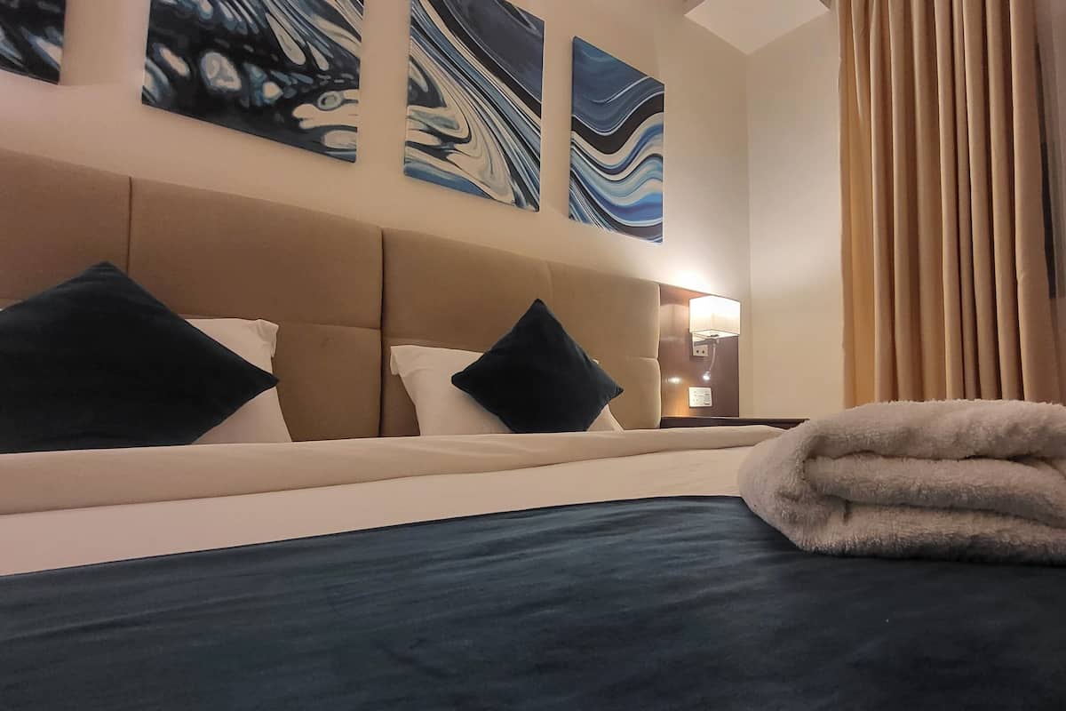 Habitación de hotel con cama, cabecera y tres cuadros abstractos en la pared.