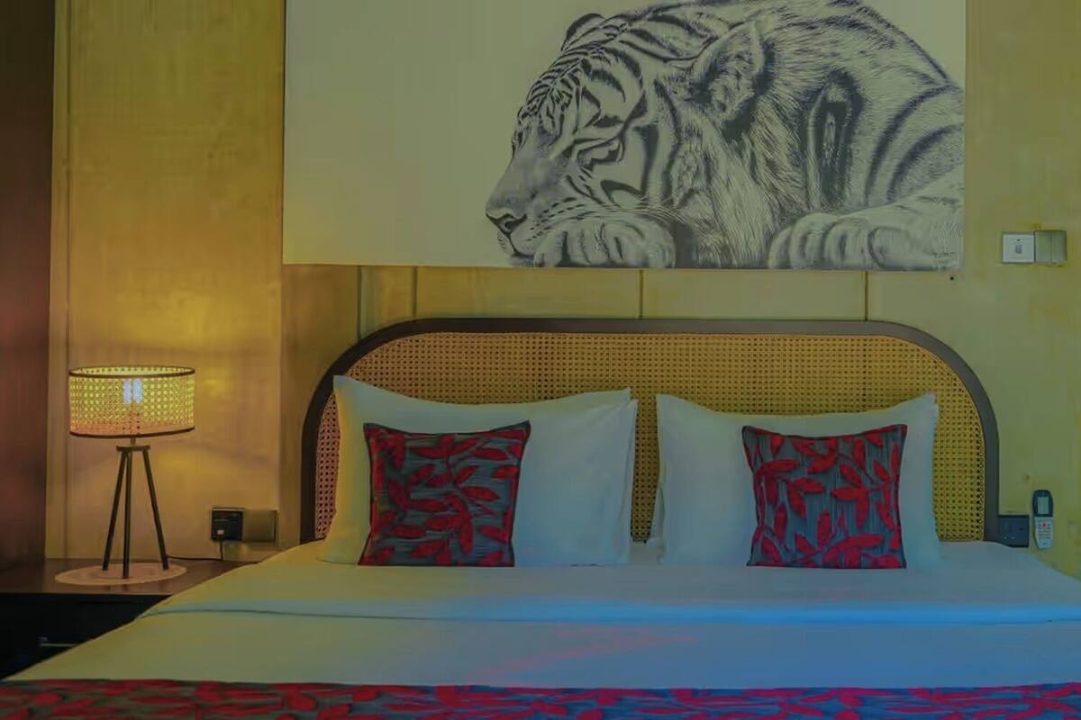 Habitación de hotel con cama, un cuadro de tigre colgado en la pared, lámpara de noche y baño a la vista a través de una puerta abierta.