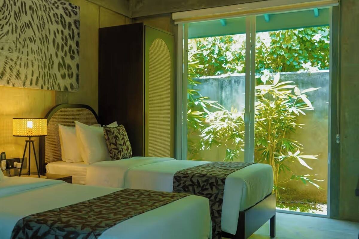 Habitación de hotel con dos camas, un ventanal con vistas a zonas verdes y una obra de arte colgada en la pared.