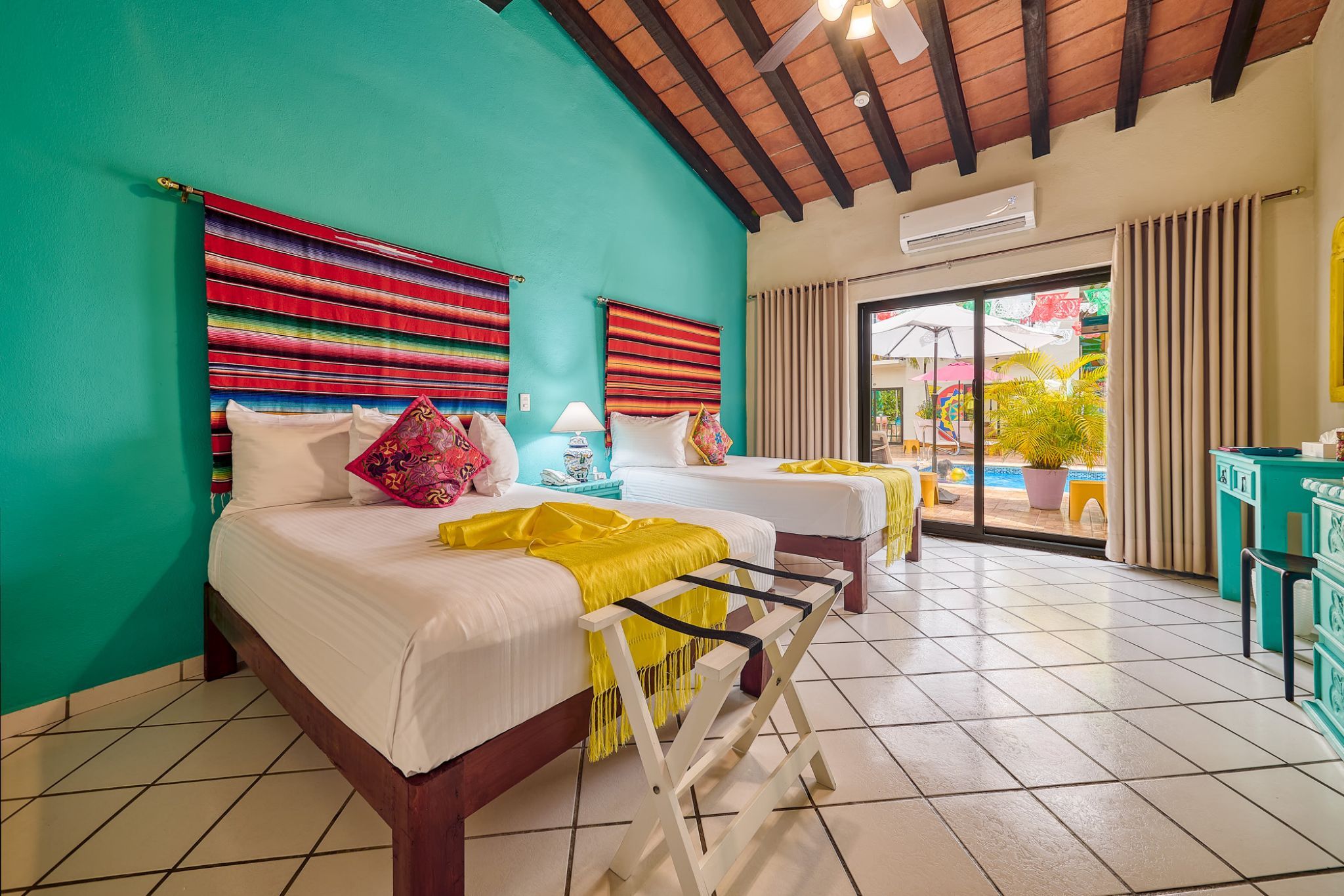 A room with two beds, a ceiling fan, a window with curtains, and a view of the outside.