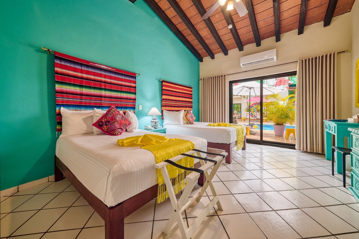 A room with two beds, a ceiling fan, a window with curtains, and a view of the outside.