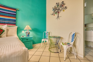 A bedroom with a bed, a nightstand, a lamp, a chair, a small table, and a wall decoration. - Casa Maria Hotel Vallarta (Puerto Vallarta)