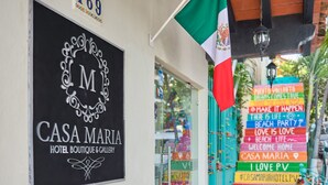 Schild für 'CASA MARIA HOTEL BOUTIQUE & GALLERY' mit dekorativem Emblem und einem Straßenschild mit verschiedenen Hinweisen.