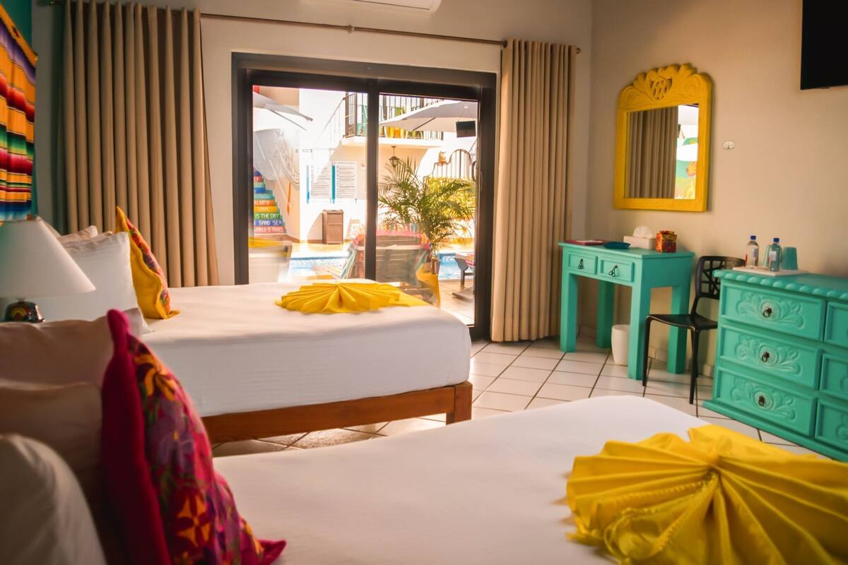 A hotel room with a bed, a desk, a mirror, and a view of the outside.