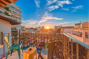 A balcony with chairs and a table, overlooking a cityscape with buildings and a sunset. - Casa Maria Hotel Vallarta (Puerto Vallarta)