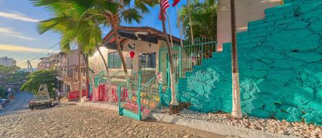 Une rue pavée de pierres, un véhicule, un bâtiment avec un mur turquoise et un palmier.