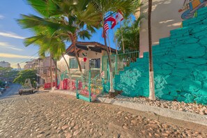 Eine Straße mit Kopfsteinpflaster, ein Fahrzeug, ein Gebäude mit einer türkisblauen Wand und eine Palme.