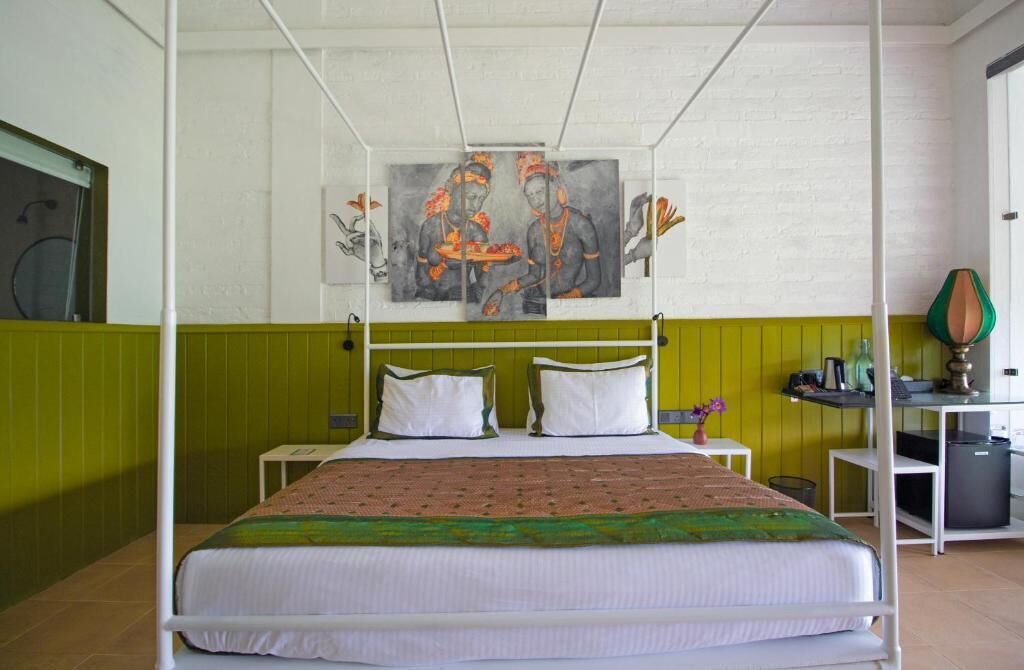 Ein Zimmer mit einem Bett, einer grünen Wand, einem Gemälde und einem Schreibtisch mit Lampe.