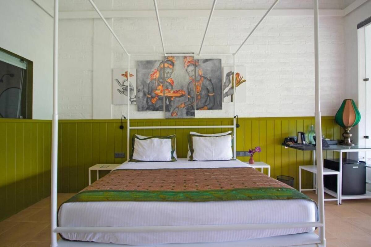 Et værelse med en seng, grøn væg, et maleri og et skrivebord med en lampe.