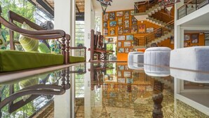 A room with a glass table reflecting the interior, a staircase with a mural, and a green cushioned chair. - Amba Yaalu - Thema Collection (Kandalama)