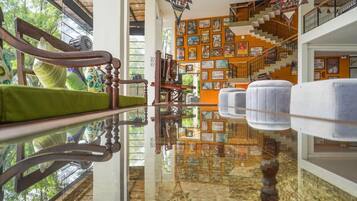 Una habitación con una mesa de vidrio que refleja el interior, una escalera con un mural, y una silla verde acolchada.