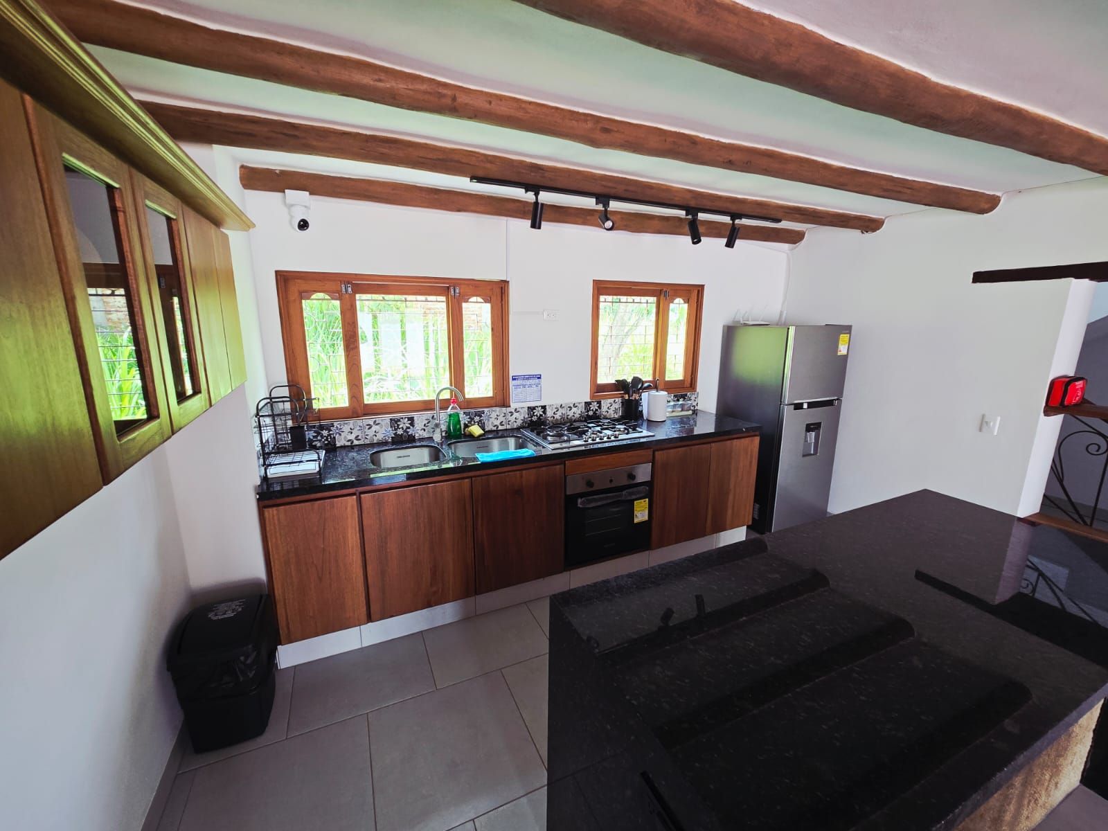 Una cocina con armarios de madera, un refrigerador de acero inoxidable y un ventanal con vistas a la vegetación.
