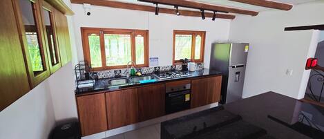 Una cocina con armarios de madera, un refrigerador de acero inoxidable y un ventanal con vistas a la vegetación.