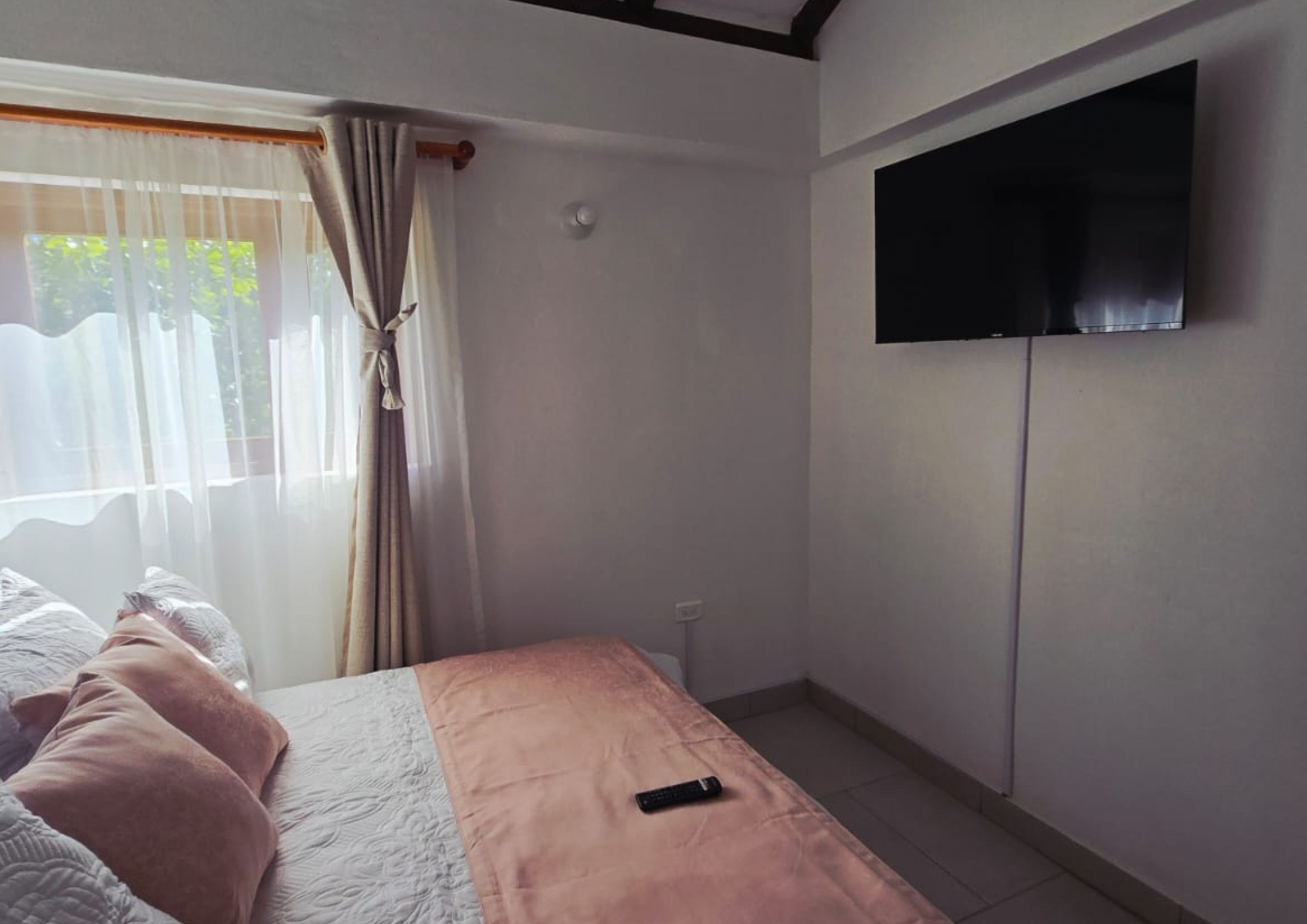 A bedroom with a bed, a TV mounted on the wall, and a window with curtains.