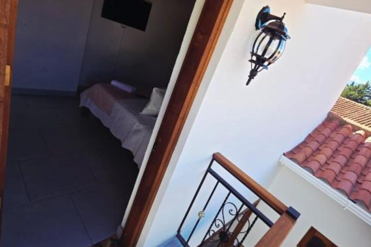 Una habitación con cama, una ventana pequeña e iluminación en la pared.